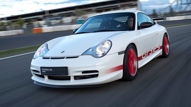 A white Porsche 911 GT3 RS with striking red wheels and decals speeds along a racetrack, the blurred background emphasizing its thrilling motion.