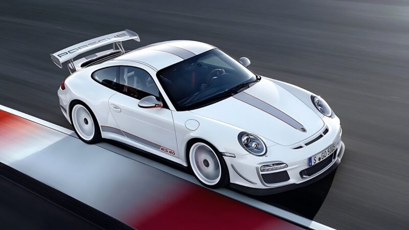 A white Porsche 911 GT3 RS with red accents and a large rear wing speeds around a racetrack.