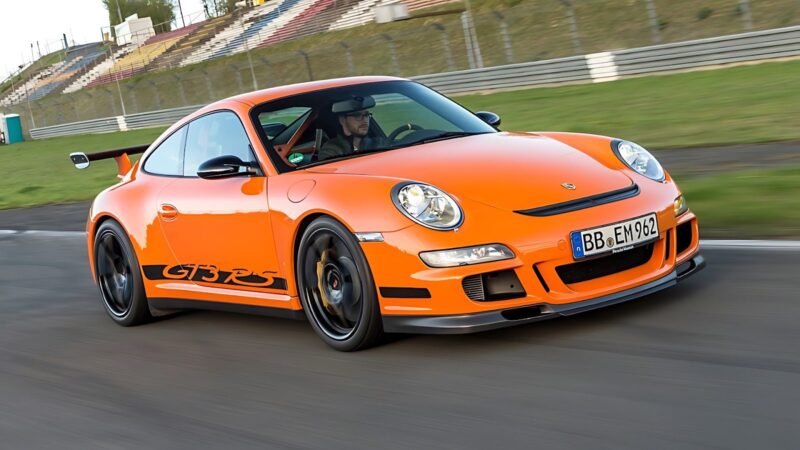 An orange Porsche 911 GT3 RS speeds around a racetrack, its blurred surroundings capturing the intense motion and power of this iconic sports car.