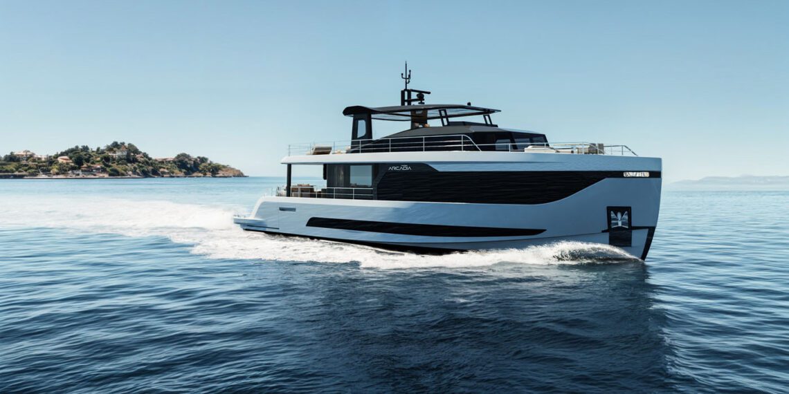 An elegant Arcadia Yachts A80new glides across calm blue water, its modern white and black design reflecting a commitment to sustainability, with a distant island visible on the left under a clear sky.