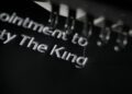 Close-up of a black fabric being machine embroidered with the words "Majesty The King" in white thread, reminiscent of the elegance found in a New Aston Martin or an exquisite Royal Warrant.