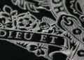 Close-up of an intricate silver embroidery design featuring floral patterns and the text "DIEU ET" on a dark fabric background, reminiscent of the elegance found in the interiors of an Aston Martin.