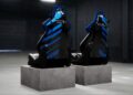 Two black and blue racing-style gaming chairs, inspired by an Automobili Pininfarina collaboration, are placed on separate concrete blocks in a dimly lit, industrial setting.