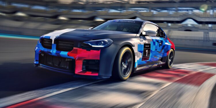 A BMW M2 Racing car with geometric blue and red graphics speeds along a racetrack, approaching a corner as the blurred stands rush by in the background.