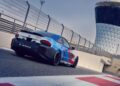 A BMW M2 Racing car with a blue and red livery is parked on a racetrack near a modern tower structure and safety barriers.