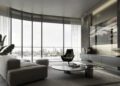 Modern living room with floor-to-ceiling windows, gray furniture, a round coffee table, and a city skyline view—perfectly suited for luxury real estate in Abu Dhabi. A large TV is mounted on the wall opposite the sofa.