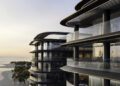 Modern multi-story building with large glass balconies overlooking a sandy beach and palm trees at sunset, offering a glimpse of luxury real estate living on exclusive BRABUS Island in Abu Dhabi.