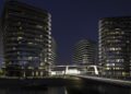 Three modern, multi-story buildings with curved balconies are illuminated at night on BRABUS Island in Abu Dhabi, connected by a bridge over the water—showcasing the pinnacle of luxury real estate.