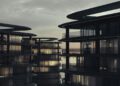 Modern multi-story buildings with curved glass facades are shown at dusk on BRABUS Island in Abu Dhabi, their interior lights aglow beneath a cloudy sky—an inviting glimpse into the world of luxury real estate.