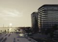 Modern beachfront buildings on BRABUS Island overlook a sandy beach with lounge chairs, palm trees, and a calm sea at sunset—offering the finest in Abu Dhabi luxury real estate.