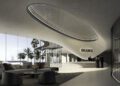 Modern, minimalist lobby with curved architecture, a large oval ceiling light, "BRABUS" sign above a white reception desk, and three people interacting at the counter—an ideal setting for luxury real estate on BRABUS Island in Abu Dhabi.