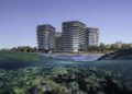 Modern beachfront high-rise buildings line the Abu Dhabi shoreline, with clear water in the foreground revealing underwater coral reefs—offering a glimpse into true Luxury Real Estate.