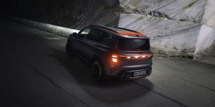 A dark-colored SUV, boasting an impressive 637HP by BRABUS, cruises with illuminated taillights through a dimly lit tunnel beside a stone wall.