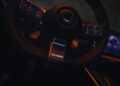 Close-up of a car steering wheel with "Brabus" on the center. The 637HP steering wheel features buttons, and the smart car's interior displays a lit screen in the background.