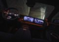 The car interior boasts a modern dashboard with three touch screens showcasing various interfaces. The steering wheel, equipped with controls, complements the ambient lighting and sleek design of this smart vehicle by BRABUS.