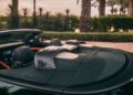 Close-up of the interior and rear section of a Bentley Batur Convertible with carbon fiber roll bars, palm trees reflected on the surface, and lush Dubai greenery in the background.