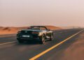 A Bentley Batur Convertible makes its public debut as it cruises along an empty desert highway in Dubai under a clear sky.