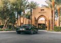A Bentley Batur Convertible, gleaming in black, is parked on a driveway in front of the Bab Al Shams entrance in Dubai, framed by palm trees and desert-style architecture.