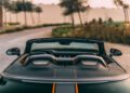 A close-up rear view of the Bentley Batur Convertible with the top down, parked on a curved road in Dubai, surrounded by trees and sand dunes, capturing its stunning look ahead of its public debut.
