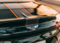 Close-up of the rear of a black Bentley car, featuring the Bentley emblem and part of the taillight with reflections on the glossy surface, captured during the new Bentley Batur Convertible’s Dubai debut.