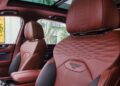 The luxury car interior boasts red leather seats with quilted patterns and a prominent emblem, embodying Bentley's bespoke craftsmanship. A sunroof and part of the door panel complete the elegant Bentayga experience.