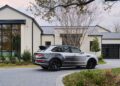 A Bentley SUV is elegantly parked on a circular driveway in front of a modern house with large windows and a metal roof. The landscaping adds charm to this serene setting, where the bespoke Victoris Bentayga finds its perfect spot among the trees.