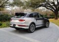 A luxury Bentley SUV is parked on a paved driveway surrounded by trees and greenery. The bespoke Bentayga, silver with a black roof, boasts modern design features.