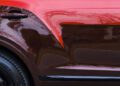 Close-up of a bespoke Bentley's side in vivid red, showcasing reflections of bare tree branches on the glossy paint.