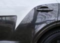 Close-up of a Bentley's rear side, showcasing its glossy, two-tone paint finish gleaming with tree reflections. The image captures the contour of the wheel arch and bespoke rear door handle, embodying the unique elegance synonymous with Bentaygas.