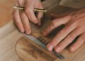 Close-up of a person using a pencil and metal ruler to mark measurements on a wooden surface labeled “BENTLEY”—part of an Otter Surfboards and Bentley surfboard collaboration.