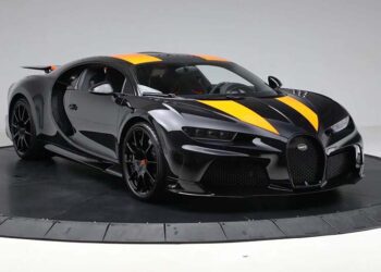 A black Bugatti sports car, one of the most expensive hypercars, with orange racing stripes is displayed in a studio setting with a plain background.
