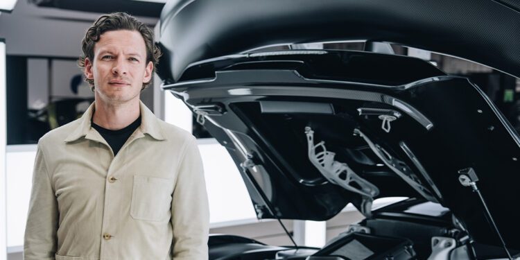 George Biggs stands next to a high-performance McLaren, its rear engine cover open to reveal the impressive mechanical components.