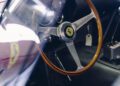 Close-up view of a classic Ferrari 330 LM/250 GTO steering wheel with wood trim, dashboard gauges, a gear shift, and a hanging key tag, captured inside the car at the Cavallino Classic.