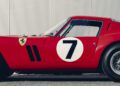 Side view of a classic red Ferrari 330 LM/250 GTO race car with a white circle and number 7 on the door, Ferrari logo on the fender, wire-spoke wheel, and a corrugated metal wall—captured at the 2025 Cavallino Classic.