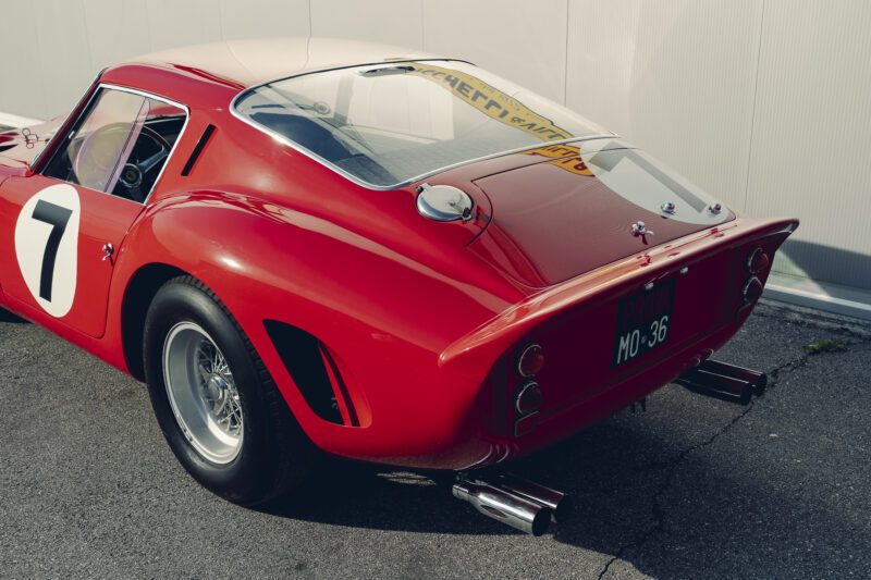 Rear view of a classic red Ferrari 330 LM/250 GTO with racing number 7, chrome exhaust pipes, and green license plate "MO-36," parked on pavement at the 2025 Cavallino Classic.