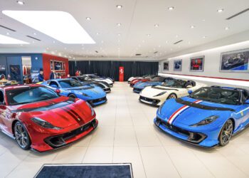 A showroom featuring an exhibition of luxury sports cars, including the stunning Ferrari 812 Competizione in red, blue, and white. The well-lit room boasts framed photos on the walls, enhancing the elegant atmosphere.