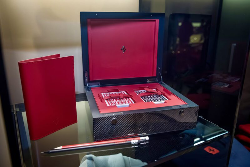 Luxury box set with two watches, red interior, and a red notebook displayed on a sleek glass shelf. A pen is stylishly positioned in the foreground, evoking the aesthetic of a Ferrari 812 Competizione cruising through New Jersey's scenic routes.