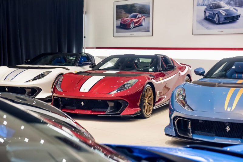Several sports cars, including red, white, and blue Ferrari models, grace a Central New Jersey showroom. The space is adorned with framed car photos on the walls, offering a perfect backdrop for showcasing the sleek elegance of each vehicle.