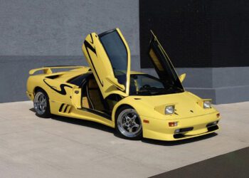 A yellow Lamborghini Diablo with scissor doors open, parked on a concrete surface in front of a gray and black wall—a true gem among collector cars.