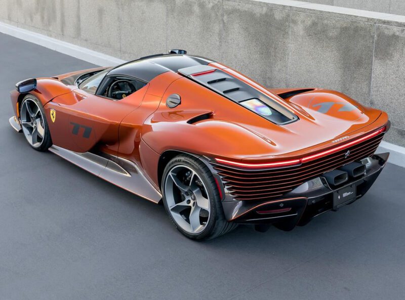A sleek orange Ferrari sports car with an aerodynamic design, distinctive rear lighting, and prominent wheel arches, parked against a concrete wall in Beverly Hills.