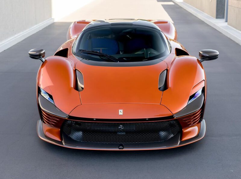 A sleek orange Ferrari sports car with aerodynamic design features and a wide front grille is parked on a gray surface, reminiscent of a Daytona SP3 scene in Beverly Hills.
