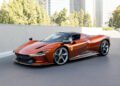 A sleek, metallic orange Ferrari Daytona SP3 sports car with aerodynamic design is parked on a city street in Beverly Hills, surrounded by tall buildings and trees.
