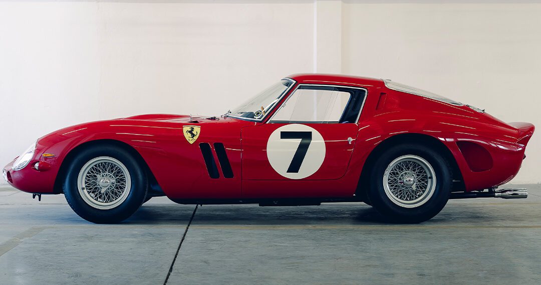 Side view of a classic red Ferrari 330 LM/250 GTO race car with the number 7 on the door, parked indoors against a white wall adorned with wireframe car sketches above—an elegant tribute ahead of Cavallino Classic 2025.
