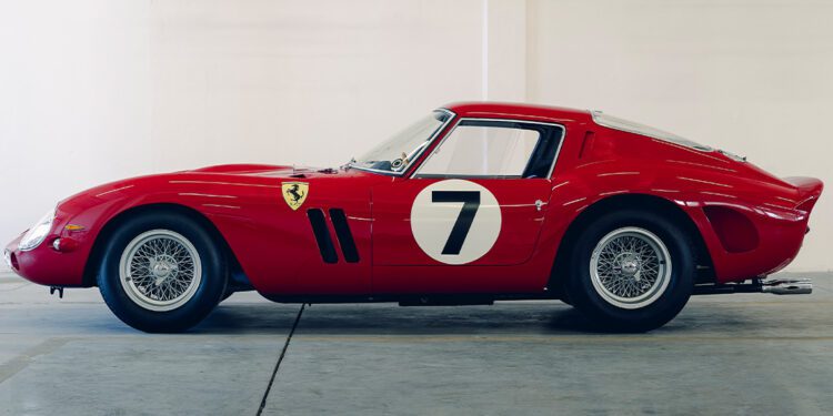 Side view of a classic red Ferrari 330 LM/250 GTO race car with the number 7 on the door, parked indoors against a white wall adorned with wireframe car sketches above—an elegant tribute ahead of Cavallino Classic 2025.