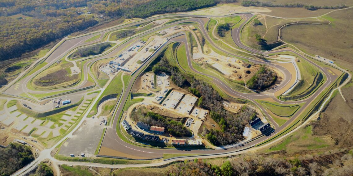 Aerial view of the Flatrock Motorclub racetrack amidst a hilly landscape, with buildings and parking areas surrounded by trees and open fields.