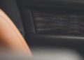 Close-up of a Bentley interior showcasing intricate tan stitching on black leather with textured patterns. A portion of a perforated tan seat is visible on the left, accentuating the luxurious craftsmanship.