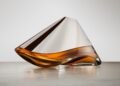 A sleek, asymmetrical glass decanter containing amber-colored Bowmore, resting on a smooth surface with a neutral background.
