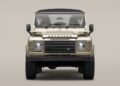 Front view of a beige Land Rover Defender Soft Top with a black roof, round headlights, and prominent "DEFENDER" badge above the grille on a plain background.