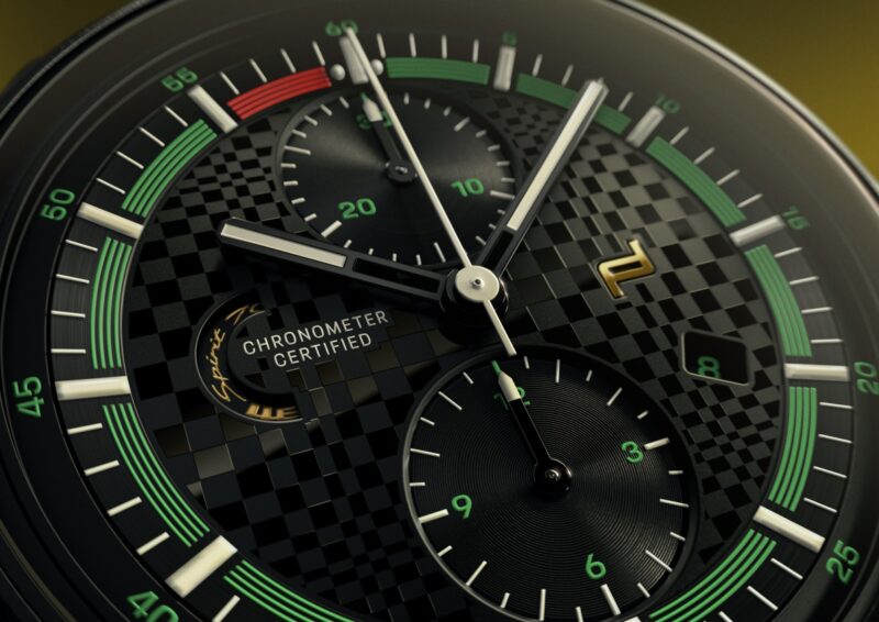 Close-up of an Owner-Exclusive Porsche Design Chronograph 911 watch face with green, white, and red accents, subdials, and a checkered pattern background.