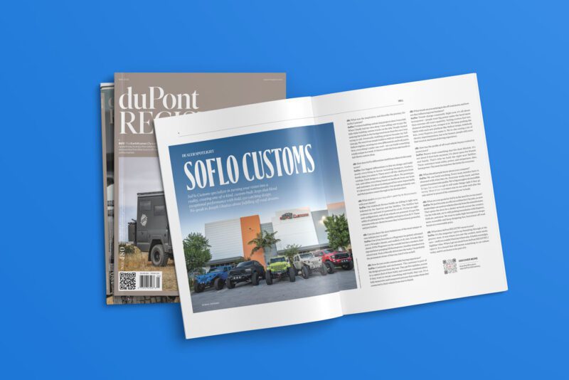 A magazine open to an article titled "SOFLO CUSTOMS" reveals text and a photo of vehicles alongside a building. Beneath it, additional magazines, including the May 2025 issue of duPont REGISTRY No. 480, are stacked against a blue background.